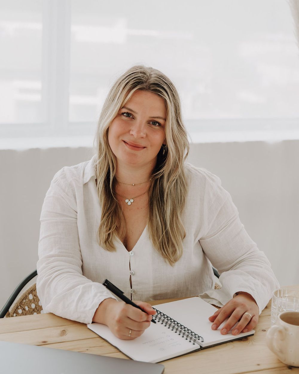 Coachin Anna Beils lächelt am Schreibtisch mit Notizbuch